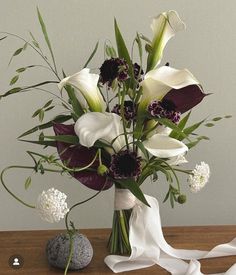 a vase filled with white and purple flowers on top of a wooden table next to a rock