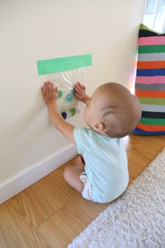 a baby sitting on the floor playing with some construction paper and glue stick art work