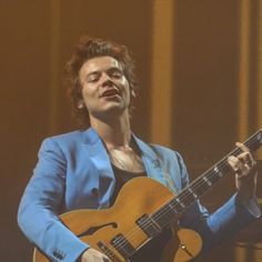 a man in a blue suit playing an acoustic guitar on stage with his eyes closed