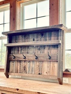 an old wooden shelf with hooks on it in front of two windows and a window sill