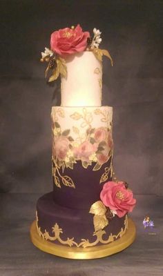 a three tiered cake with pink flowers on the top and gold trimmings