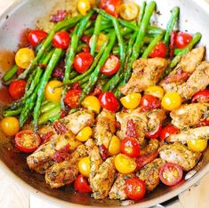 a pan filled with chicken, asparagus and cherry tomatoes