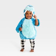 a small child dressed in a blue furry animal costume standing on one leg and smiling at the camera