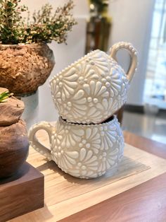 two white vases sitting on top of a wooden table next to potted plants