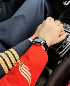 a person in uniform is driving a car with his hand on the steering wheel while wearing a watch