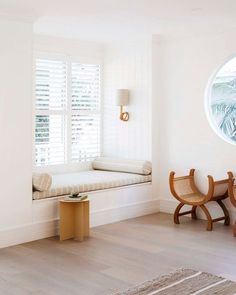 a room with white walls and wooden furniture in the corner, along with a round window that has shutters on both sides