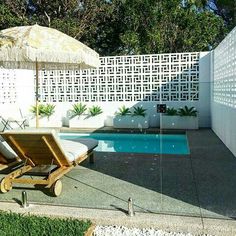 a pool with an umbrella and lounge chairs next to the swimming pool in front of it