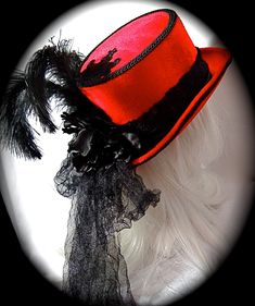 "This Gothic top hat is heavy red velvet wrapped with a black velvet and lace hatband and has a soft black crushed tulle bow & long tails in back. This Victorian style riding hat has black satin roses centered in the back. There is a silver antiqued Celtic cross centered on a beautiful black lace applique on the front of the crown. A black lace applique rests on the back of the crown's top. The brim & crown edge are trimmed in black satin braid. This hat is loaded with black curled ostri Fitted Red Halloween Hat, Fitted Red Brimmed Top Hat, Red Fitted Hat For Costume, Red Fitted Vintage Top Hat, Vintage Red Hats For Costume Party, Vintage Red Hat For Costume Party, Gothic Fitted Brimmed Top Hat, Fitted Gothic Brimmed Top Hat, Fitted Brimmed Top Hat For Costume Party