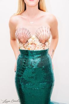 a woman wearing a green dress with seashells on it's chest and under her bra