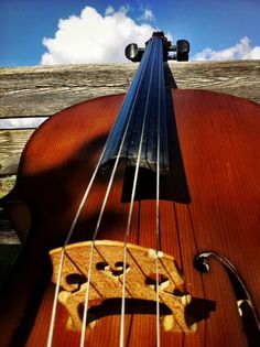 an old violin sitting on top of a wooden table next to a fence with clouds in the background