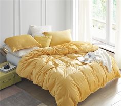 a bed with yellow comforters and pillows in a room next to a window,