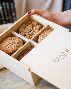 a person holding a wooden box filled with cookies and muffins on top of a table