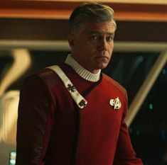 a man in a red star trek uniform looking off into the distance with his hand on his hip