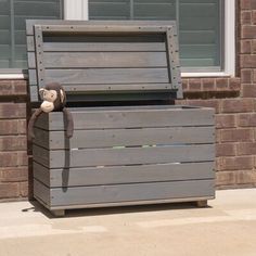 a teddy bear sitting on top of a wooden box next to a brick building with windows