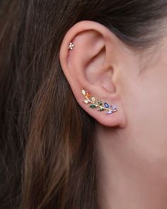 a woman wearing an ear piercing with multicolored stones on her left side and two small stars in the middle