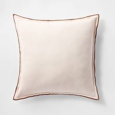 a white pillow with brown piping on the front and back, against a white wall