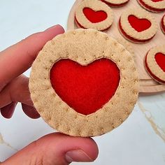 a hand holding a heart shaped cookie next to a plate of cookies with hearts on them