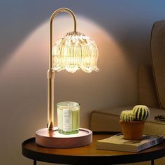 a table with a lamp on it next to a potted cactus and a book