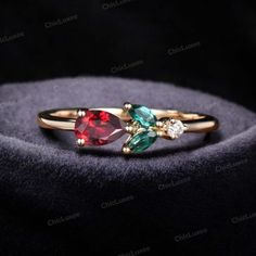 three stone ring in gold with red, green and blue stones on the side sitting on a black velvet surface