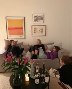 three women sitting on a couch with bottles of wine in front of them and two vases filled with flowers