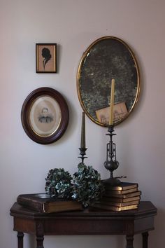 a table topped with books next to a wall mounted clock and framed pictures on the wall