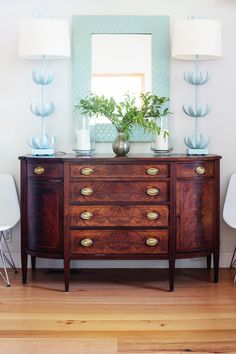 a wooden dresser sitting next to two white chairs