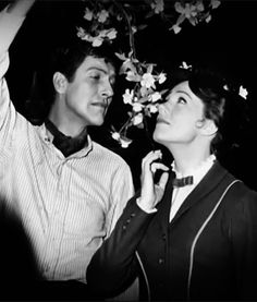 a man and woman standing next to each other in front of a tree with flowers on it