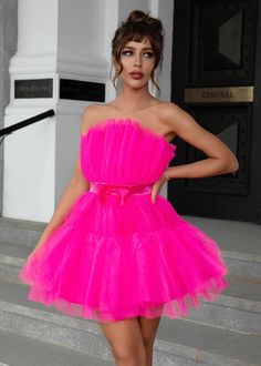 a woman in a bright pink dress posing on steps with her hands on her hips