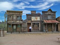 a man standing in front of an old western building with two buildings on each side