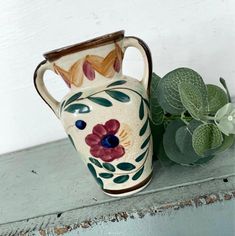 a ceramic vase sitting on top of a table next to a green leafy plant