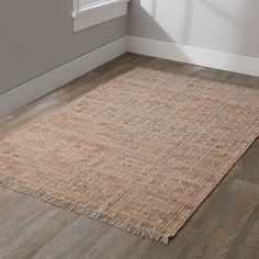 a beige rug with fringes on the floor in front of a white wall and window