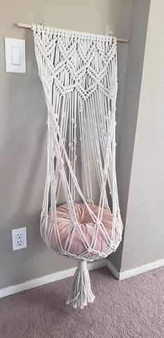 a white hammock hanging from a wall next to a light switch and pink cushion