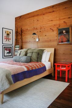 a bedroom with wood paneling on the walls and bed in front of a small red table