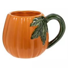 an orange ceramic mug with a green leaf on the handle and inside, is shown in front of a white background