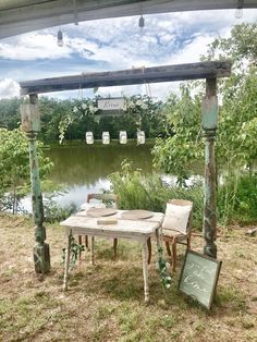 an outdoor table and chairs set up in front of a lake with greenery around it