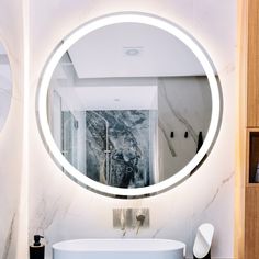 a bathroom with a large round mirror on the wall and a white tub in front of it