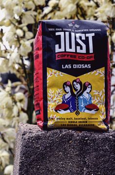 a bag of just coffee sitting on top of a cement block next to some flowers