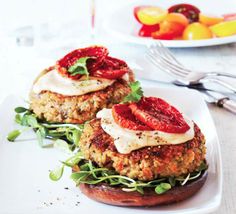 two meat patties with sauce and vegetables on a plate next to a bowl of fruit