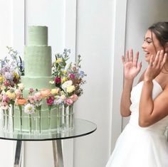 a woman standing in front of a green cake with flowers on the table next to it