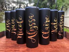 six black tumbles with gold lettering on them are lined up in a row outside