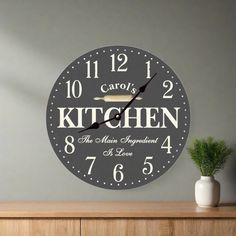 a wall clock with the words carol's kitchen on it and a potted plant next to it