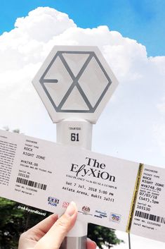 a person holding up a ticket for the exxion concert in front of a sky background