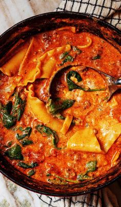 a bowl filled with pasta and spinach on top of a tablecloth next to a spoon