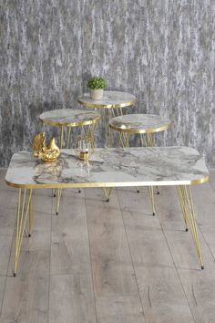 three tables with gold legs and marble top in front of a wallpapered background