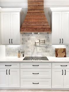 a kitchen with white cabinets and marble backsplash, wood hood over the stove