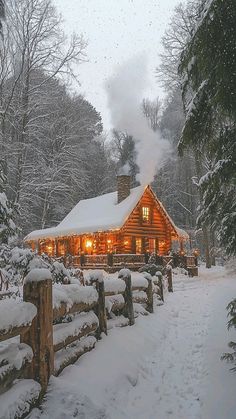 a log cabin is lit up at night in the snow with trees and fence around it