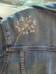 the back of a jean jacket with embroidered dandelion on it's side