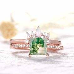 an engagement ring with a green stone surrounded by white and rose gold diamond accents, sitting on top of a table