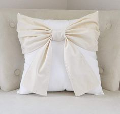 a white pillow with a large bow on the front and back of it, sitting on a couch