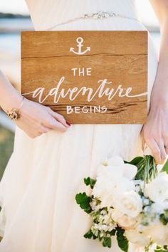 a bride holding a wooden sign that says the adventure begins with an anchor on it